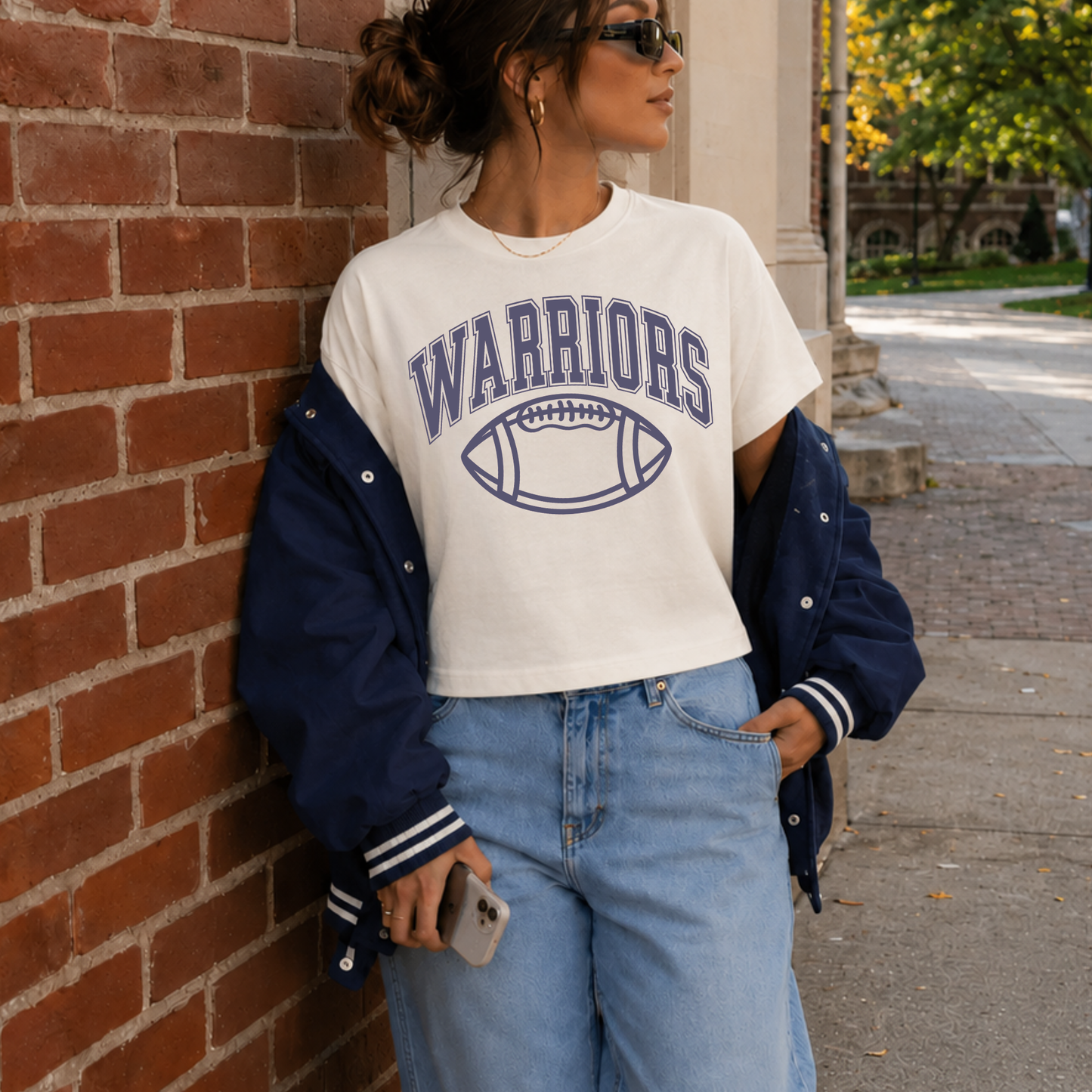 Women's Sterling Warriors football graphic cropped game day shirt with vintage athletic design paired with denim and varsity jacket.