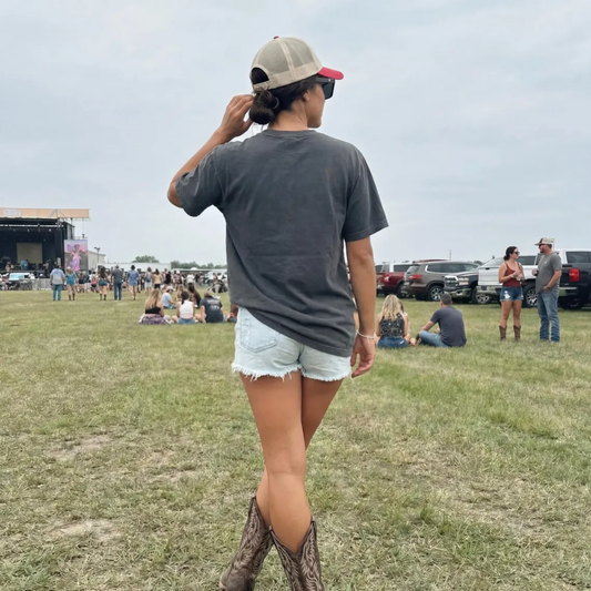 woman wearing support live music shirt from back at country concert western outfit denim shorts boots festival look
