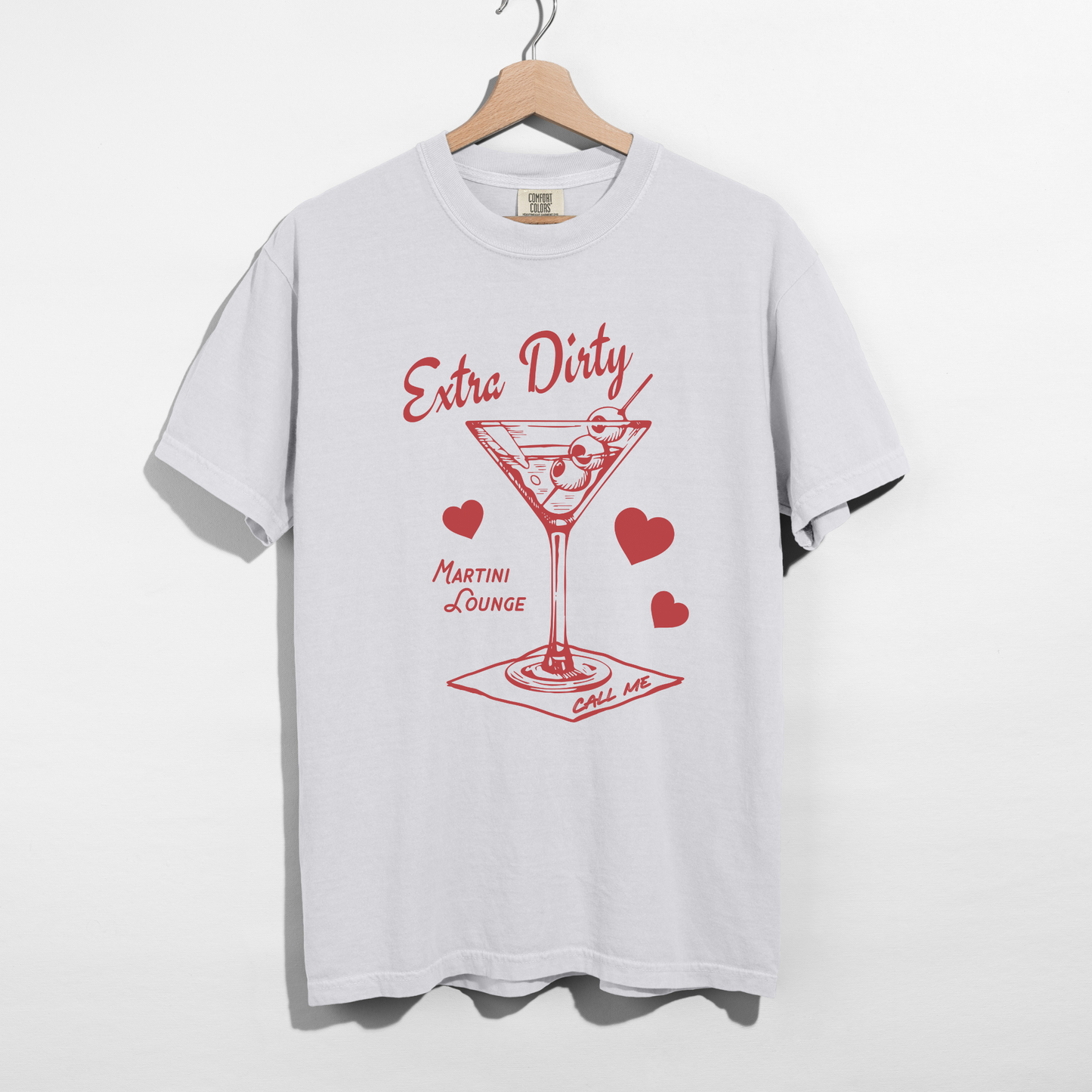 White Comfort Colors Extra Dirty Martini Lounge tee on wooden hanger against white background.