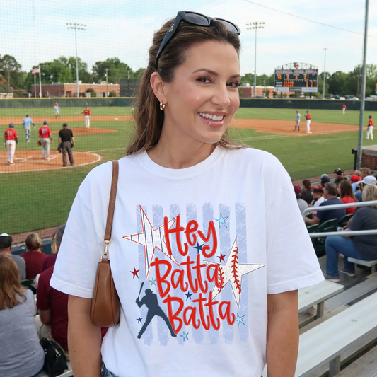 Woman wearing white Hey Batta Batta retro baseball graphic tee at outdoor baseball game stadium.