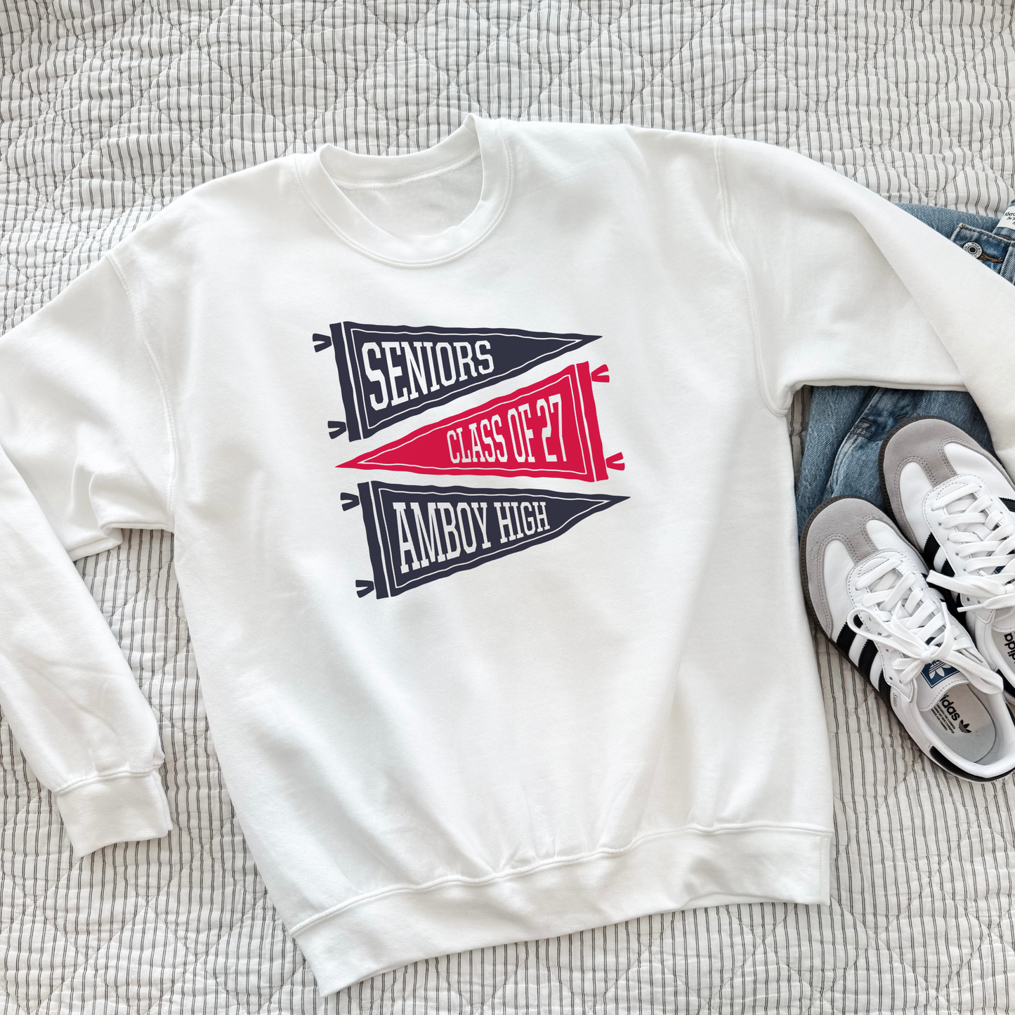 White Amboy High Seniors Class of 2027 crewneck sweatshirt with retro navy and red pennant design styled with denim jeans and sneakers.
