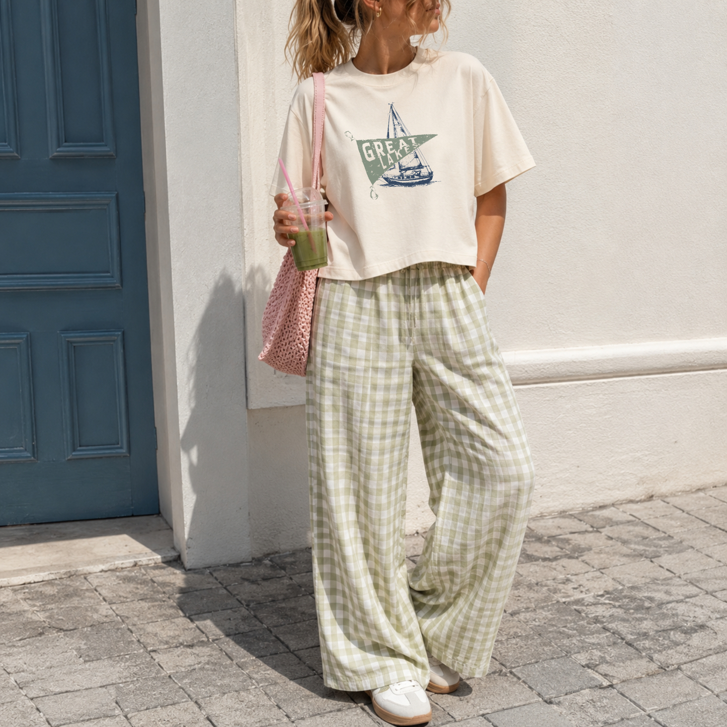 Woman wearing an ivory garment dyed boxy cropped Great Lakes graphic tee with sage gingham wide leg pants featuring a vintage sailboat and nautical pennant design.