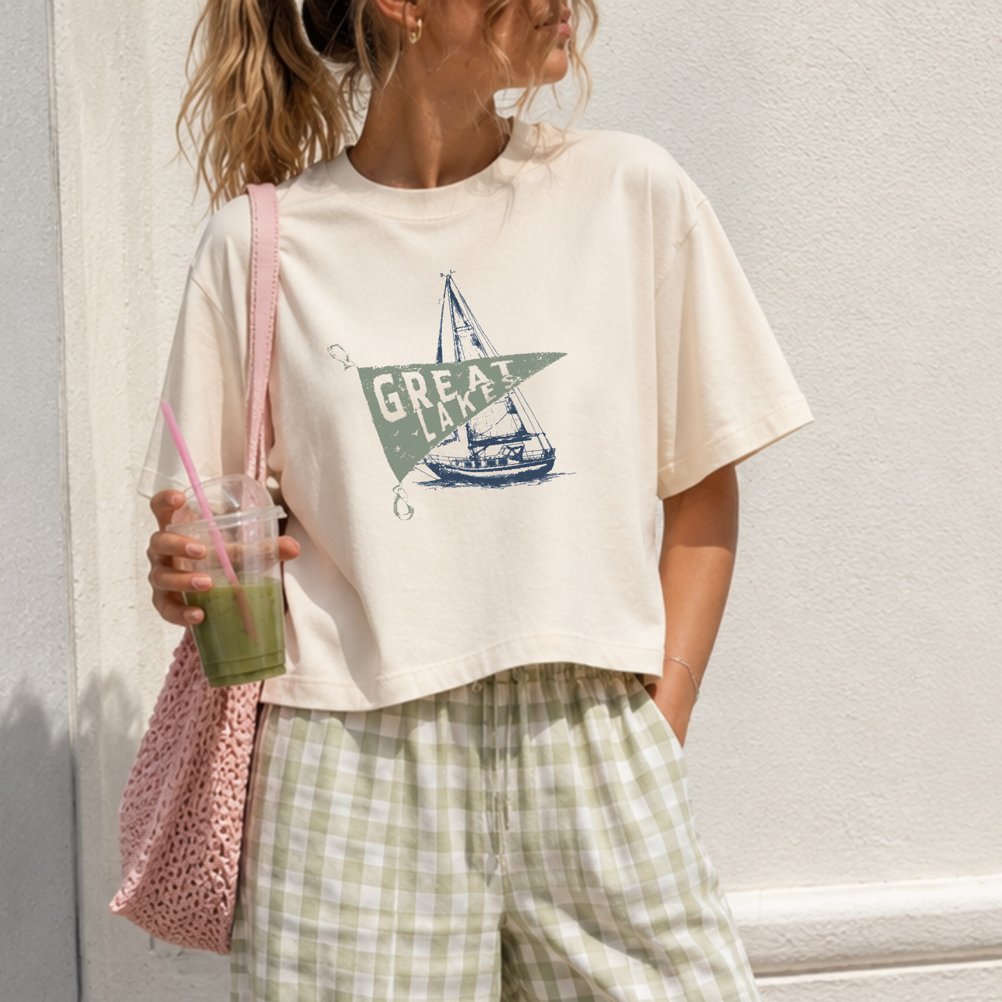 Close-up of ivory Great Lakes cropped graphic t-shirt featuring distressed sage green pennant and navy sailboat artwork on premium garment dyed cotton.