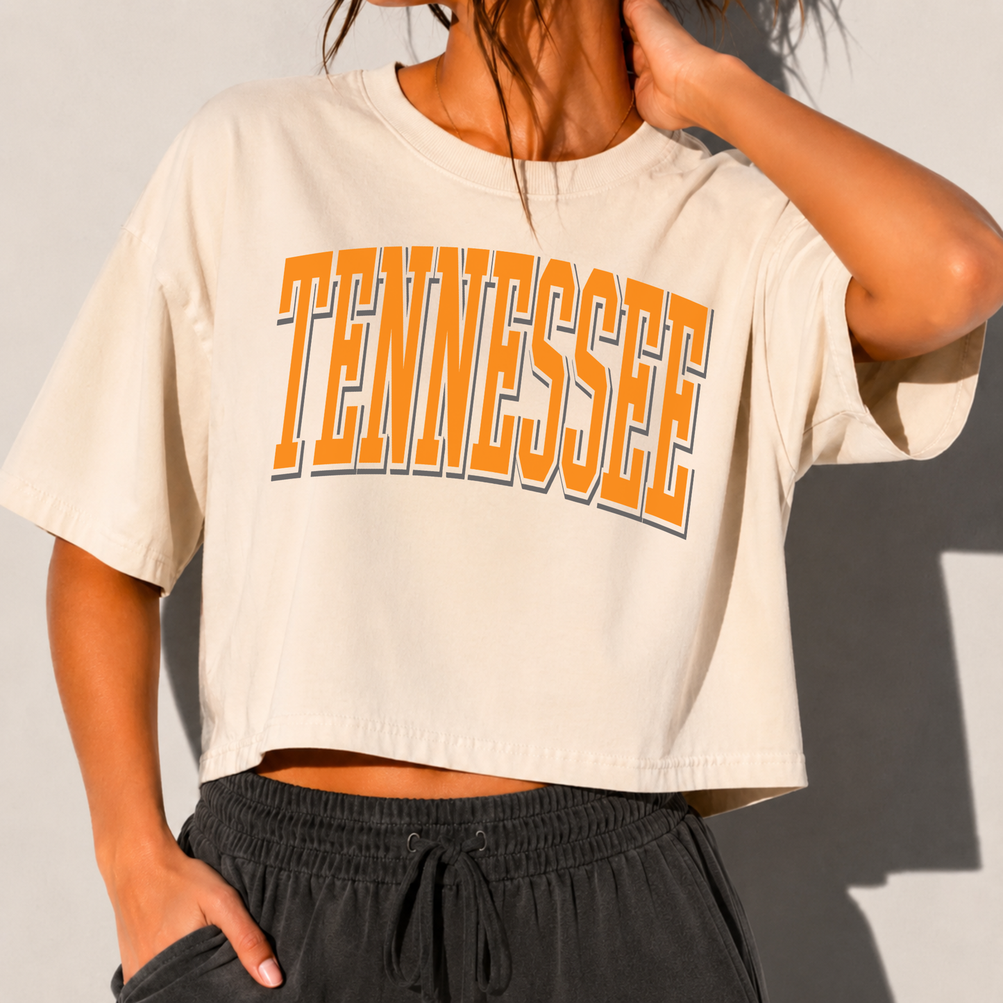 Close-up of ivory Tennessee collegiate graphic boxy crop tee featuring oversized orange varsity lettering on premium cotton fabric.