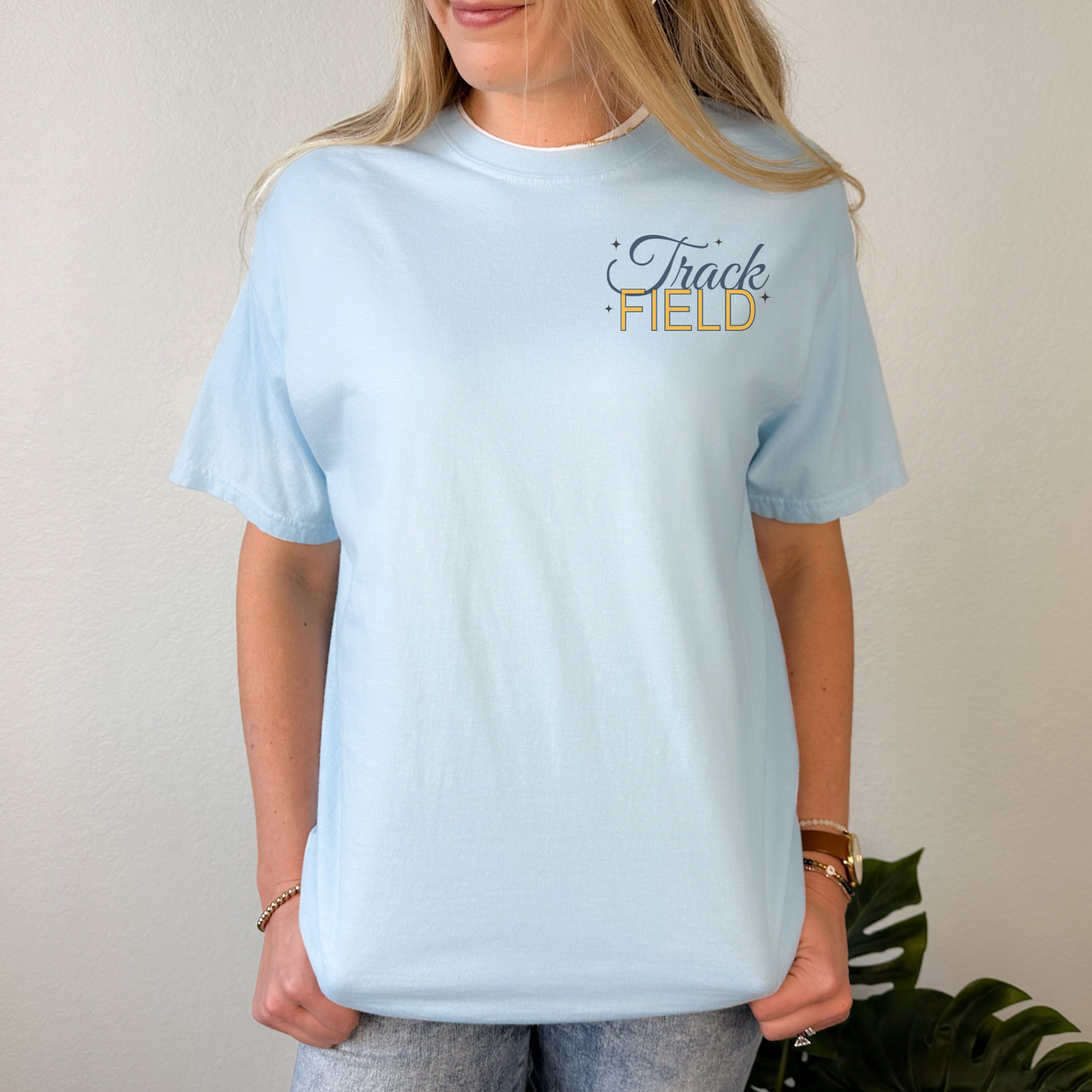 Person wearing a light blue t-shirt with 'Track Field' text on a plain background