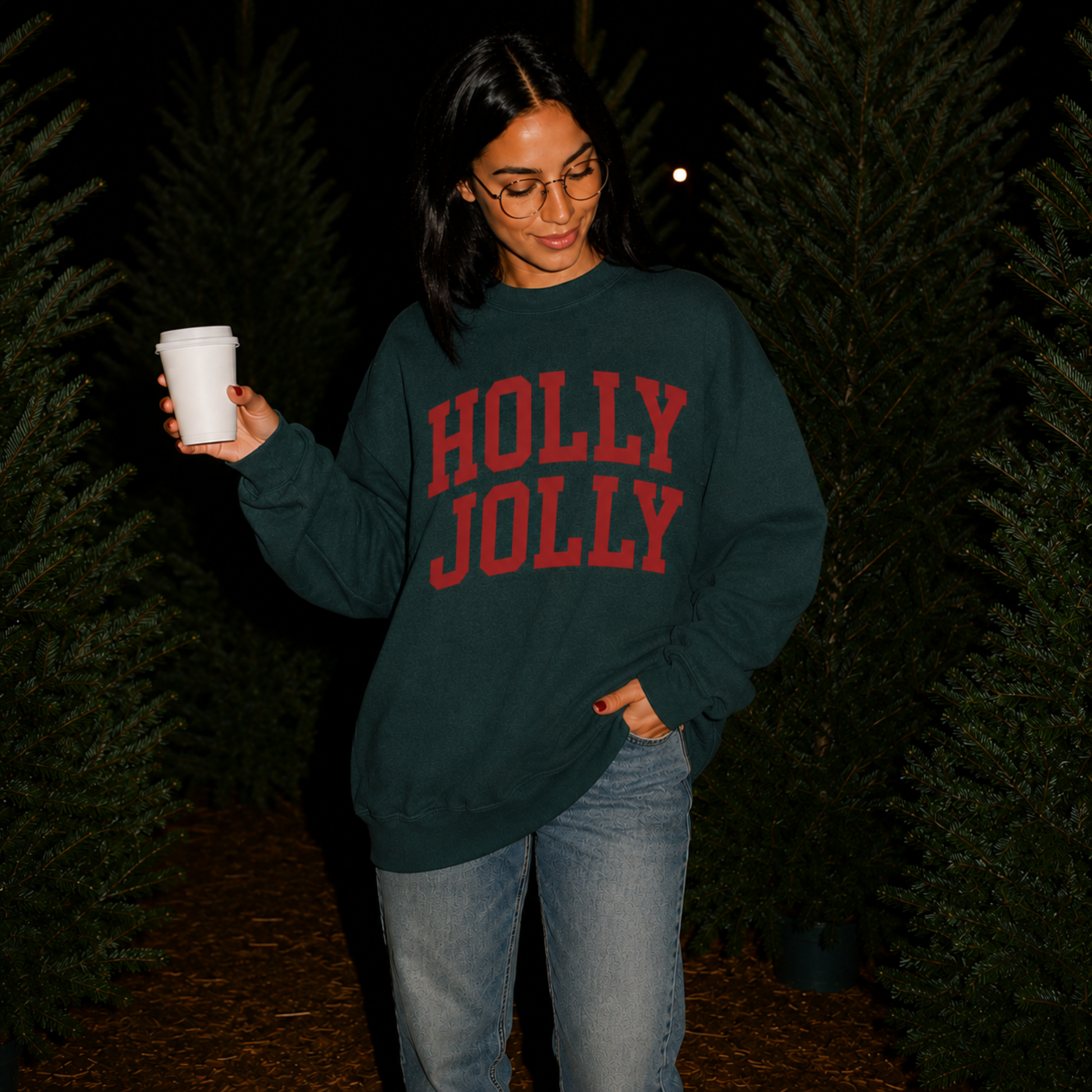 Woman wearing a forest green Holly Jolly Christmas sweatshirt with red varsity lettering while holding a coffee cup at a Christmas tree farm.