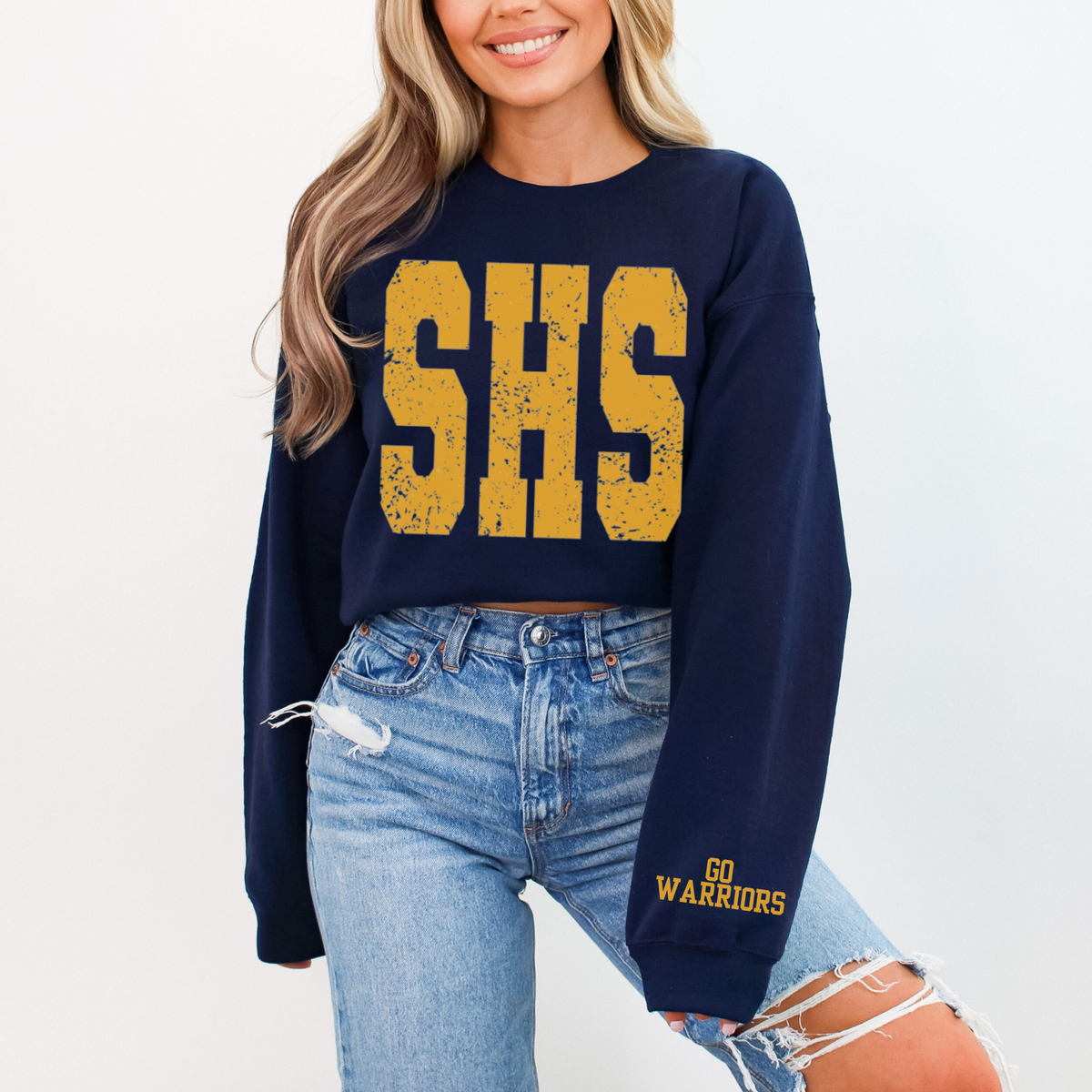 Person wearing a navy blue sweatshirt with 'SHS' in yellow and ripped jeans on a white background