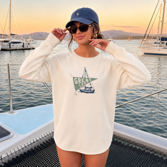 Woman wearing a bone premium Great Lakes Wave Wash crewneck sweatshirt with a vintage sailboat graphic while standing on a boat at sunset.