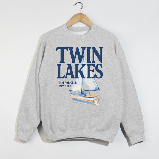 Twin Lakes Harbor Club crewneck sweatshirt featuring large navy lettering and watercolor sailboat artwork on a heather gray sweatshirt.