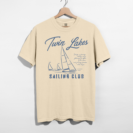 Twin Lakes Sailing Club graphic tee featuring vintage sailboat artwork and distressed navy blue nautical design on a cream Comfort Colors shirt.