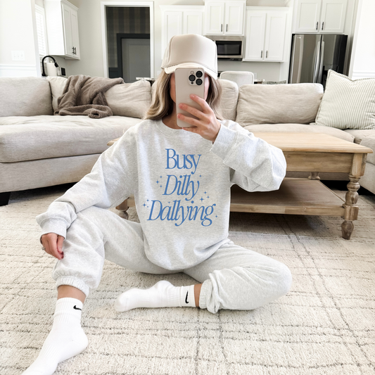 Person wearing a 'Busy Dilly Dallying' sweatshirt in a living room.