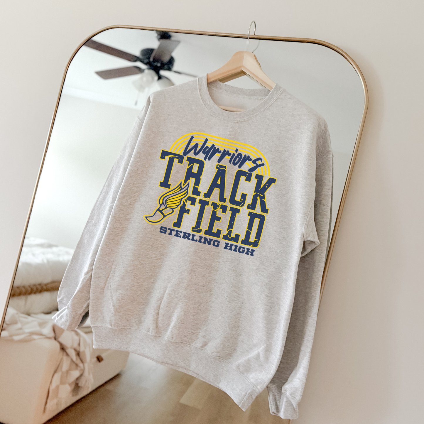 Gray Sterling High Warriors Track and Field sweatshirt hanging on a wooden hanger in a mirror with bold yellow and navy athletic graphic