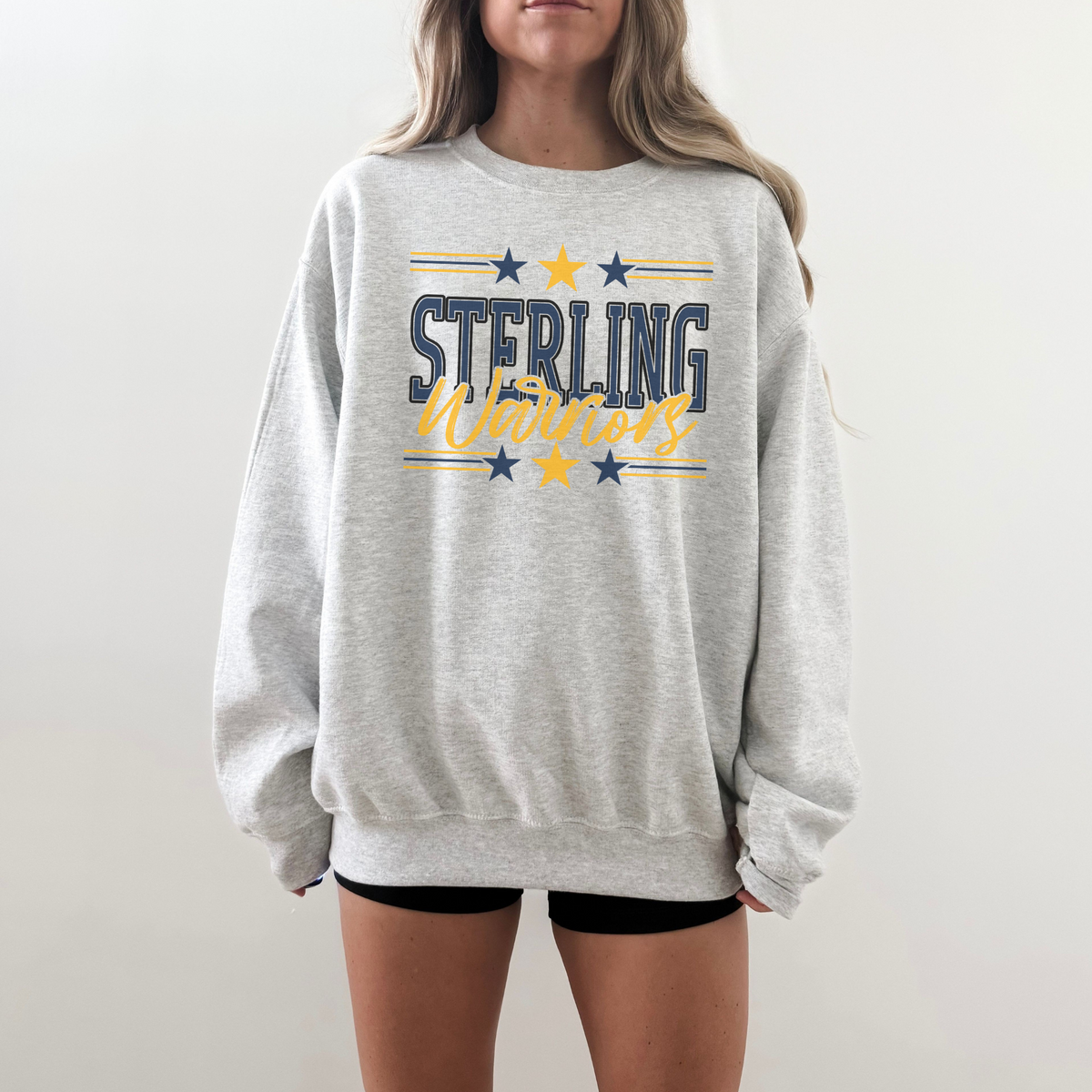Person wearing a gray sweatshirt with 'Sterling Warriors' text and stars on a plain background