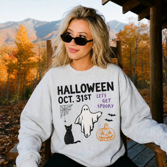 Halloween Oct. 31st ghost graphic sweatshirt featuring a black cat, pumpkin, spiderweb and bats worn outdoors during fall with colorful autumn mountains in the background.