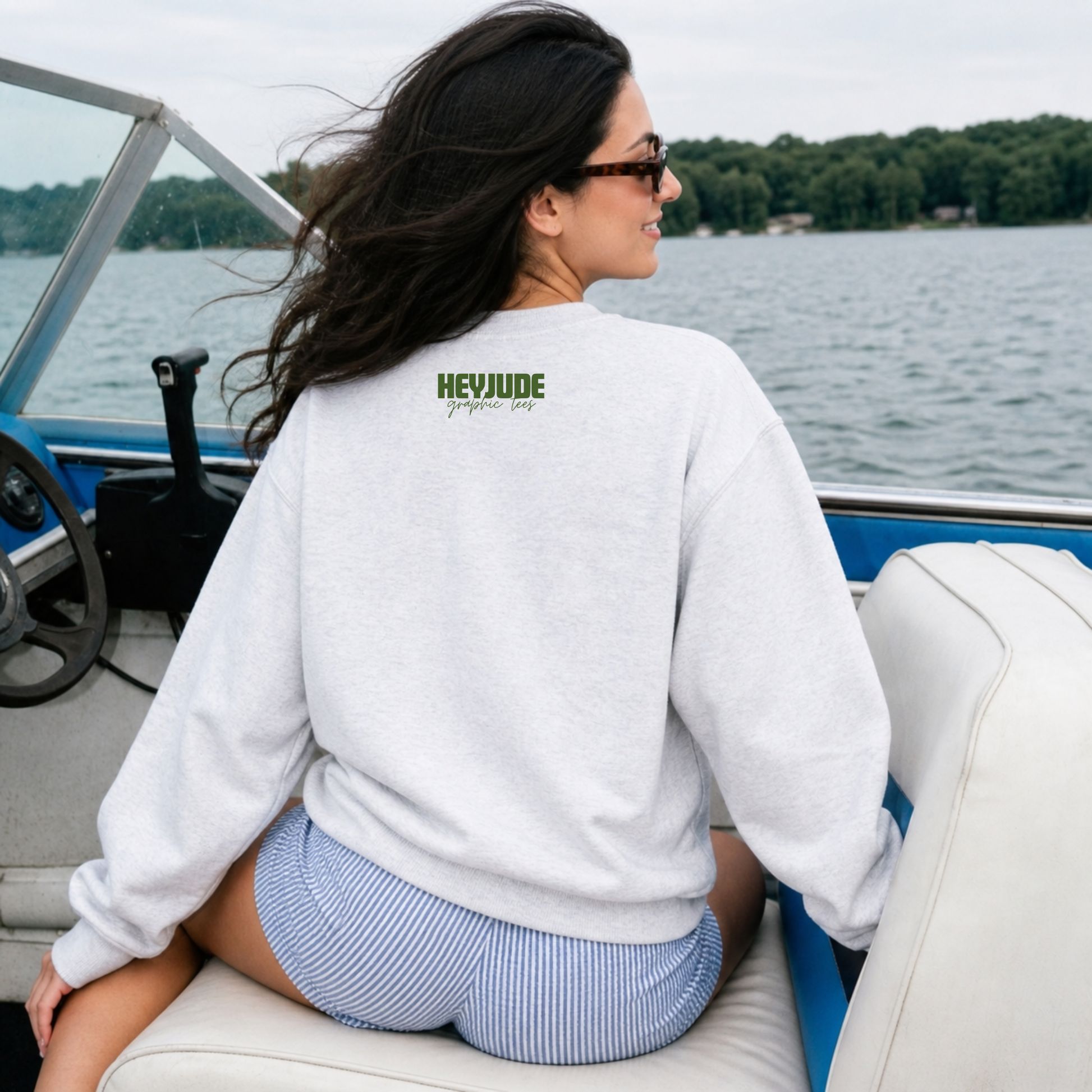 Woman on a boat wearing a white sweatshirt with a logo, looking at the water.