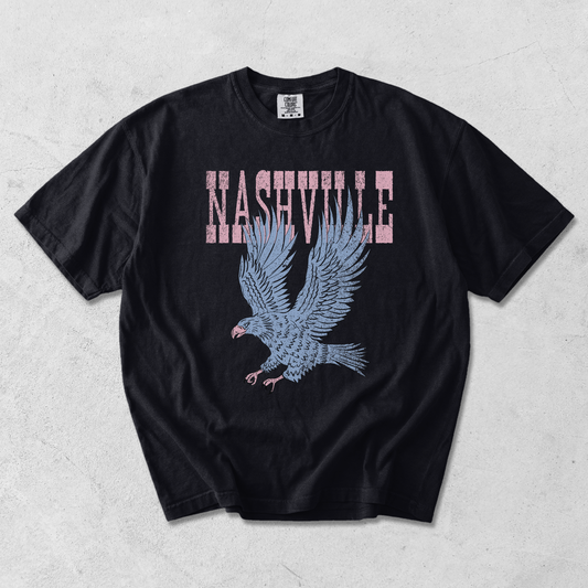 Black Comfort Colors Nashville graphic tee with distressed pink lettering and vintage blue eagle graphic on textured background.
