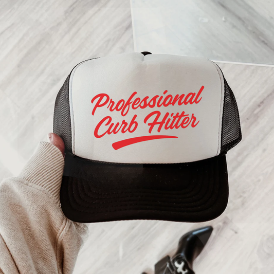 Black and white trucker hat with red “Professional Curb Hitter” text held in hand