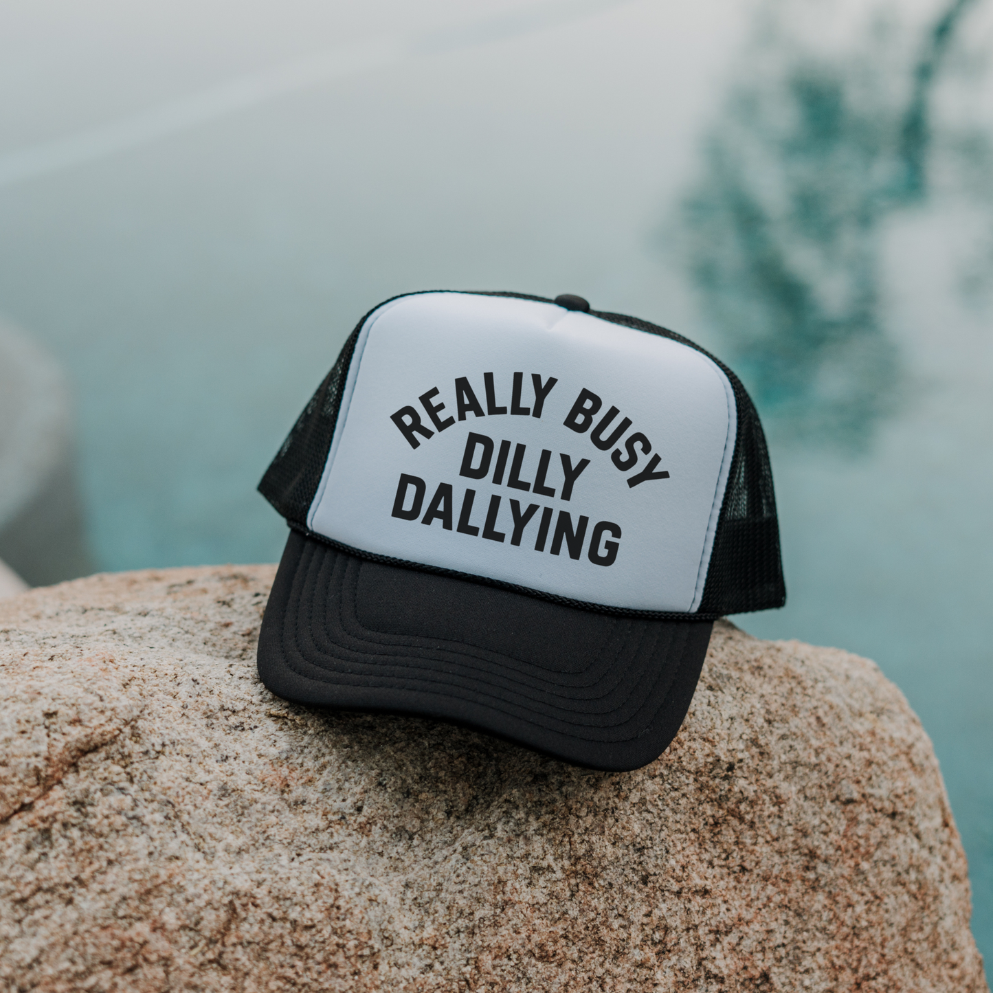 Black and white Really Busy Dilly Dallying foam trucker hat outdoors on rock