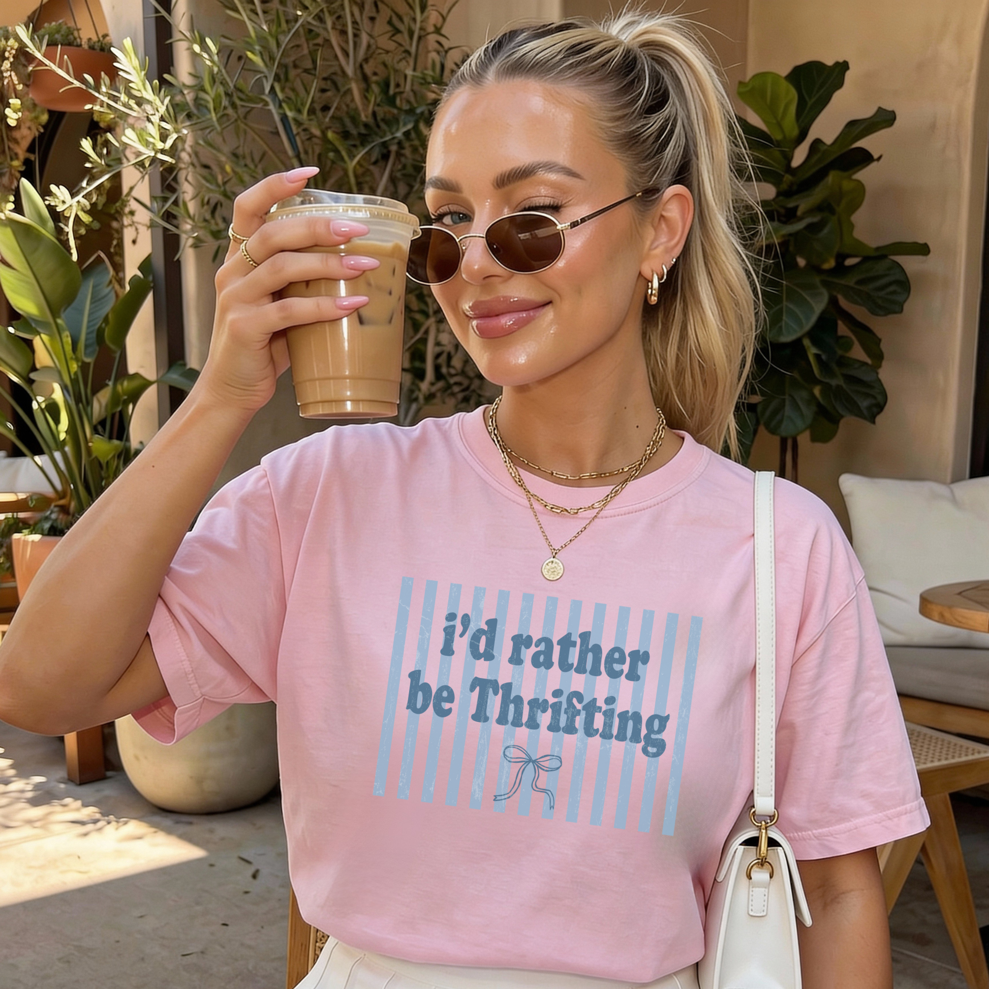 Woman wearing pink thrift-themed graphic t-shirt holding iced coffee outdoors