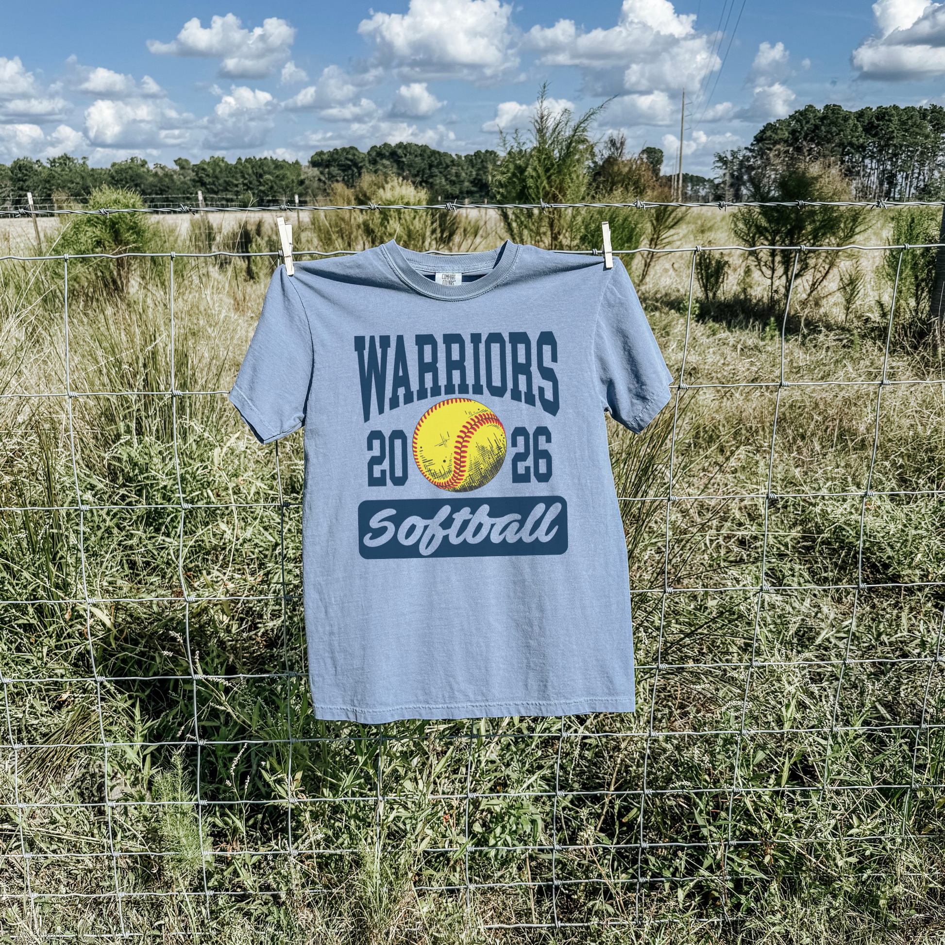 Blue jean Warriors Softball 2026 unisex school spirit shirt hanging outdoors with softball design