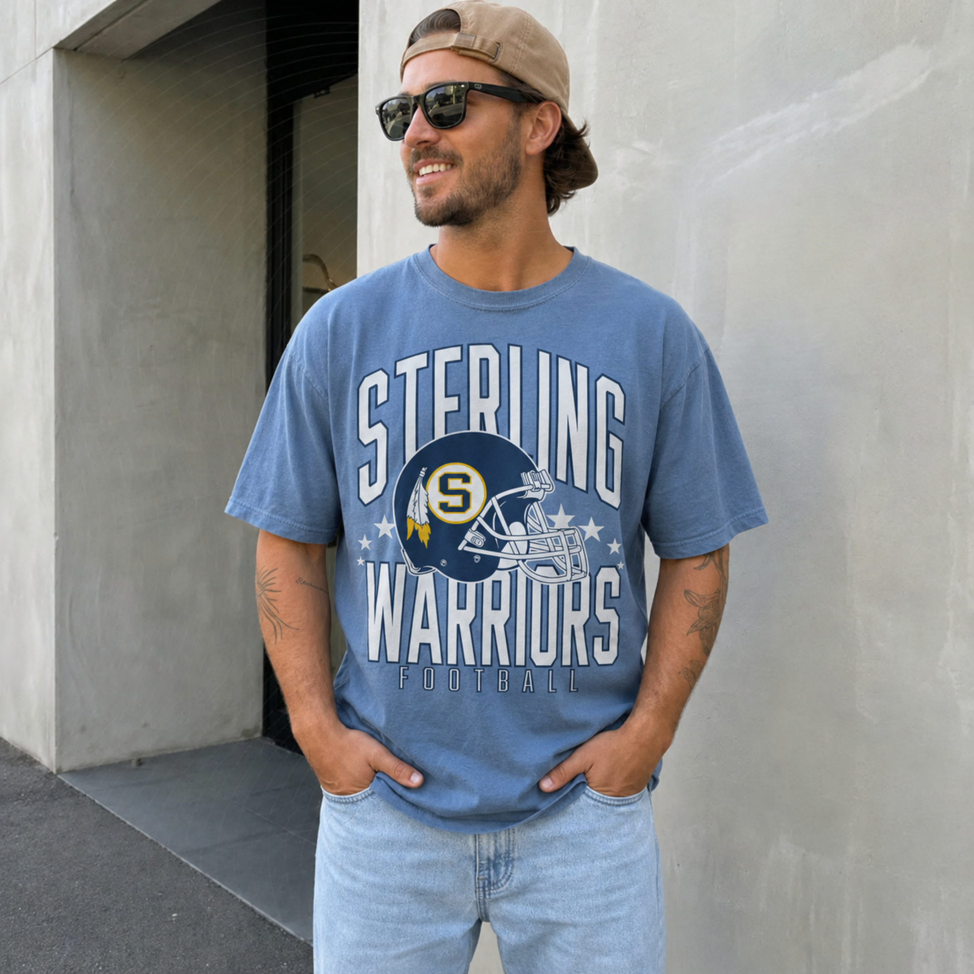 Man wearing a blue jean Sterling Warriors Football graphic t-shirt featuring a vintage football helmet and bold varsity lettering.