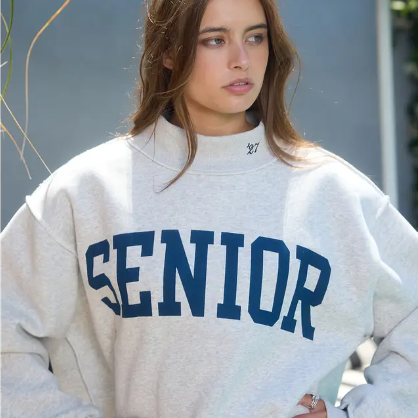 Close-up of embroidered “’27” detail on the mock neck collar of the reversible Senior sweatshirt with navy varsity lettering.