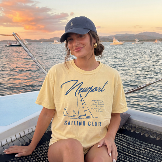 woman wearing butter yellow sailing club graphic tee on boat at sunset coastal summer outfit