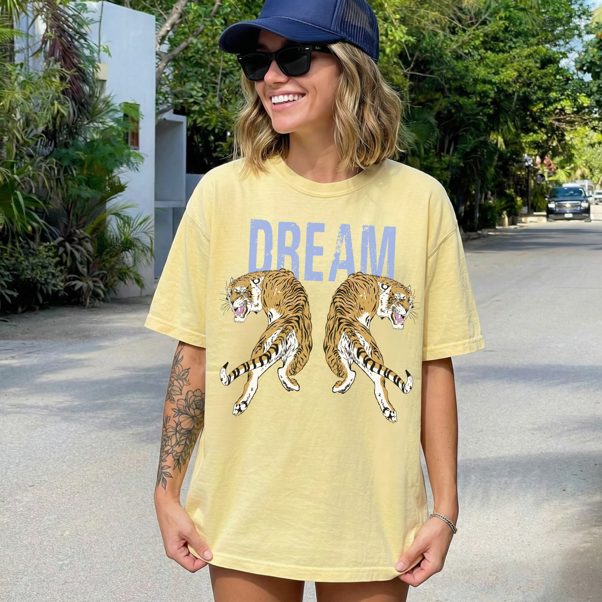 Model wearing butter yellow Dream Tiger graphic tee with blue text and mirrored tiger design outdoors