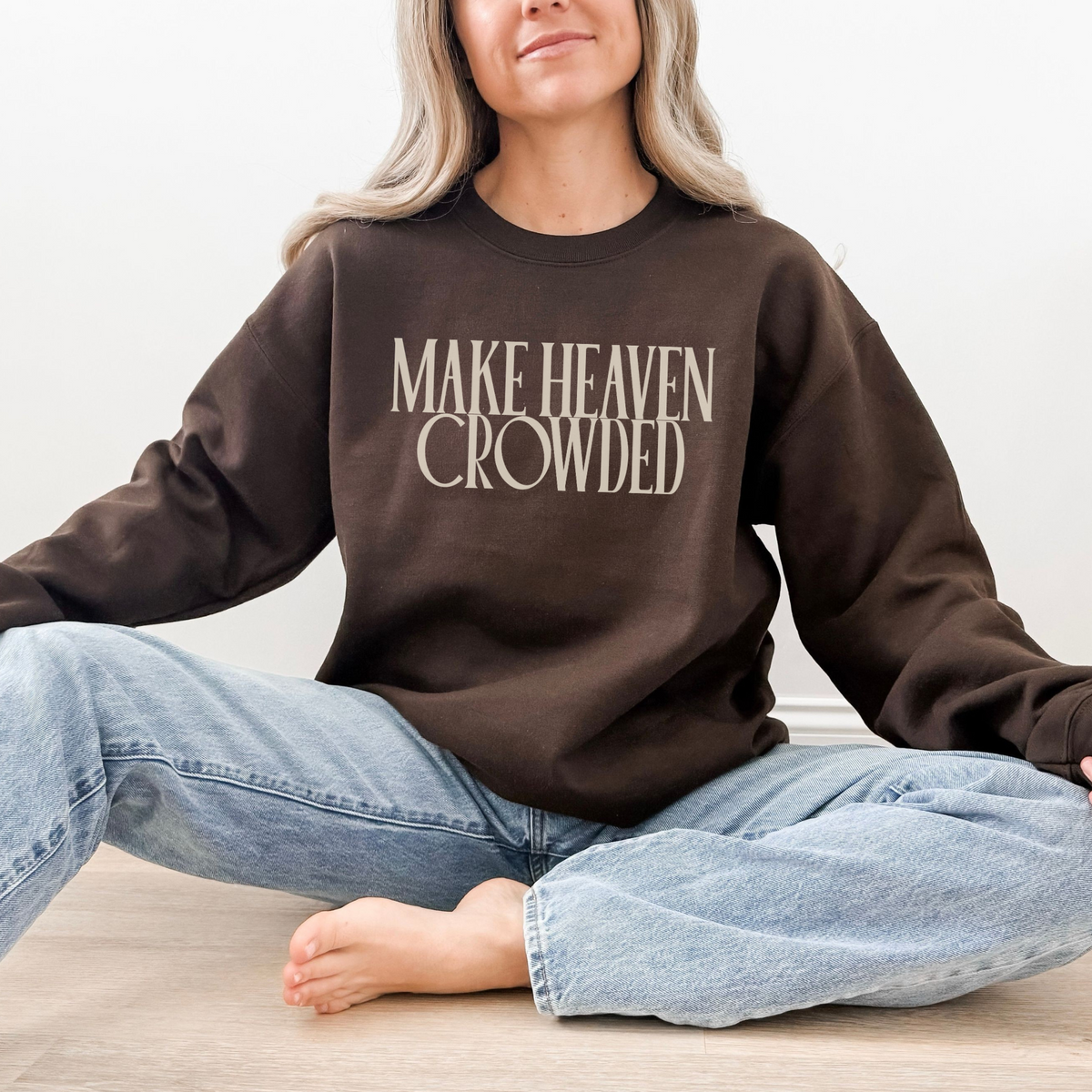 Person wearing a brown sweatshirt with 'MAKE HEAVEN CROWDED' text, sitting on a light-colored floor.