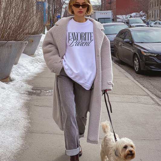 White Favorite Parent sweatshirt with black text worn by woman walking dog on city sidewalk in winter outfit