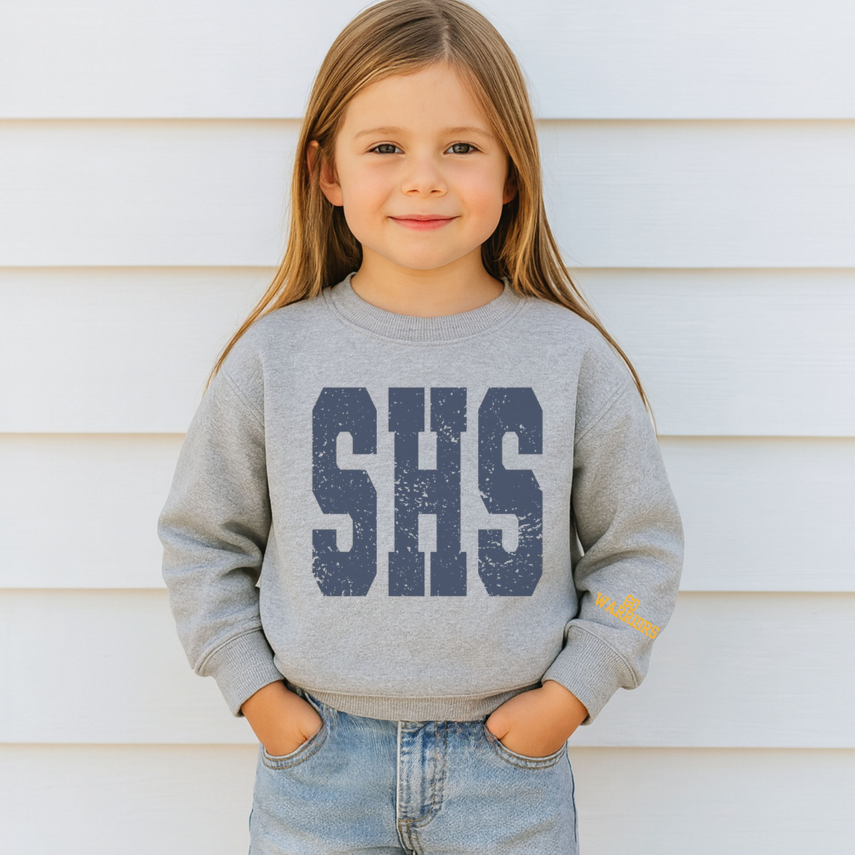 Child wearing a gray sweatshirt with 'SHS' on it against a white wall.
