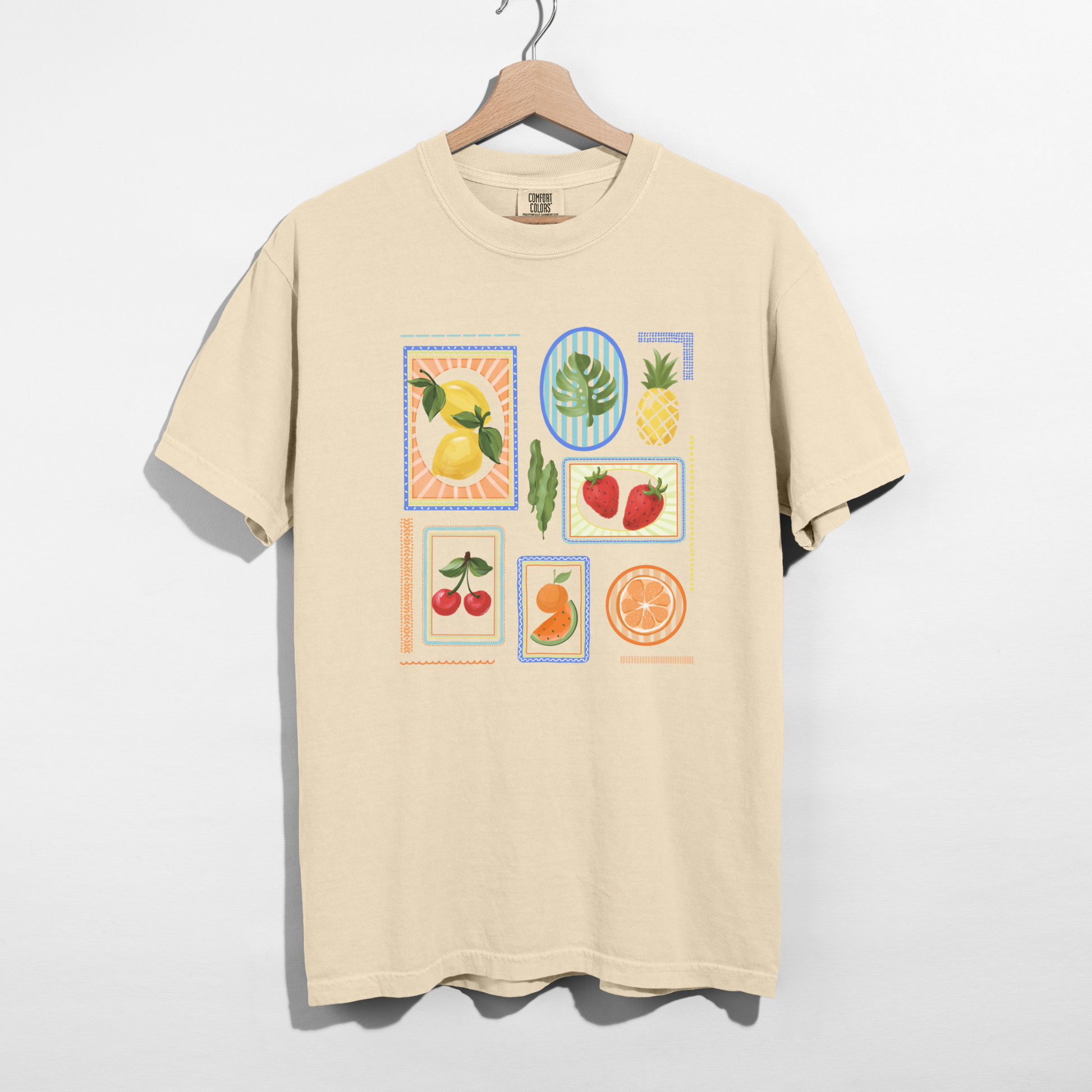 Ivory fruit block graphic tee hanging on wooden hanger against white background.