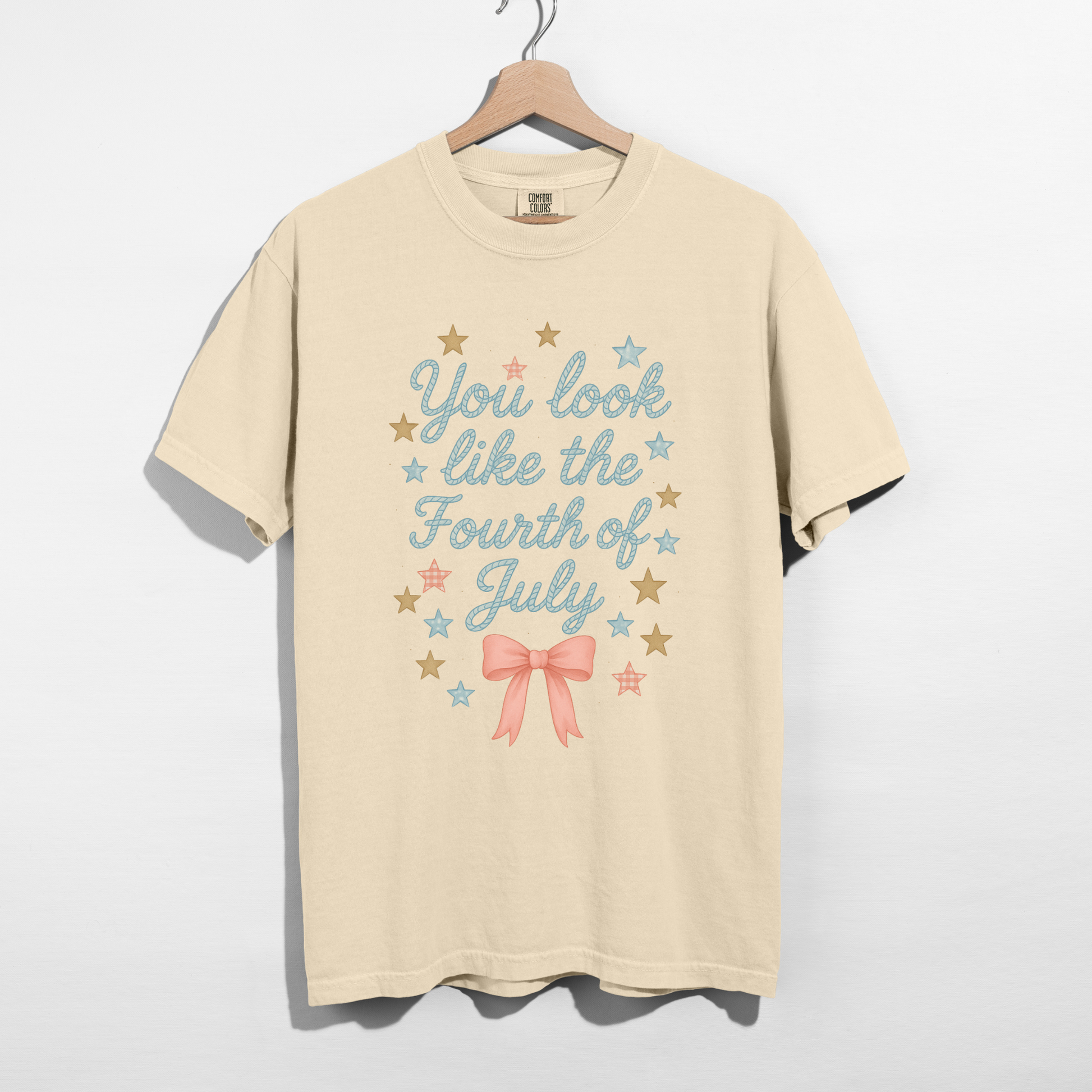 Beige t-shirt with 'You look like the Fourth of July' text and stars on a hanger against a white background