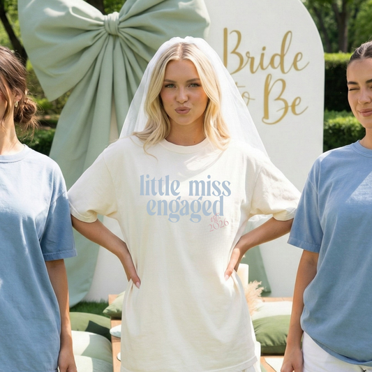 Bride wearing ivory Little Miss Engaged Est. 2026 t-shirt at outdoor engagement party
