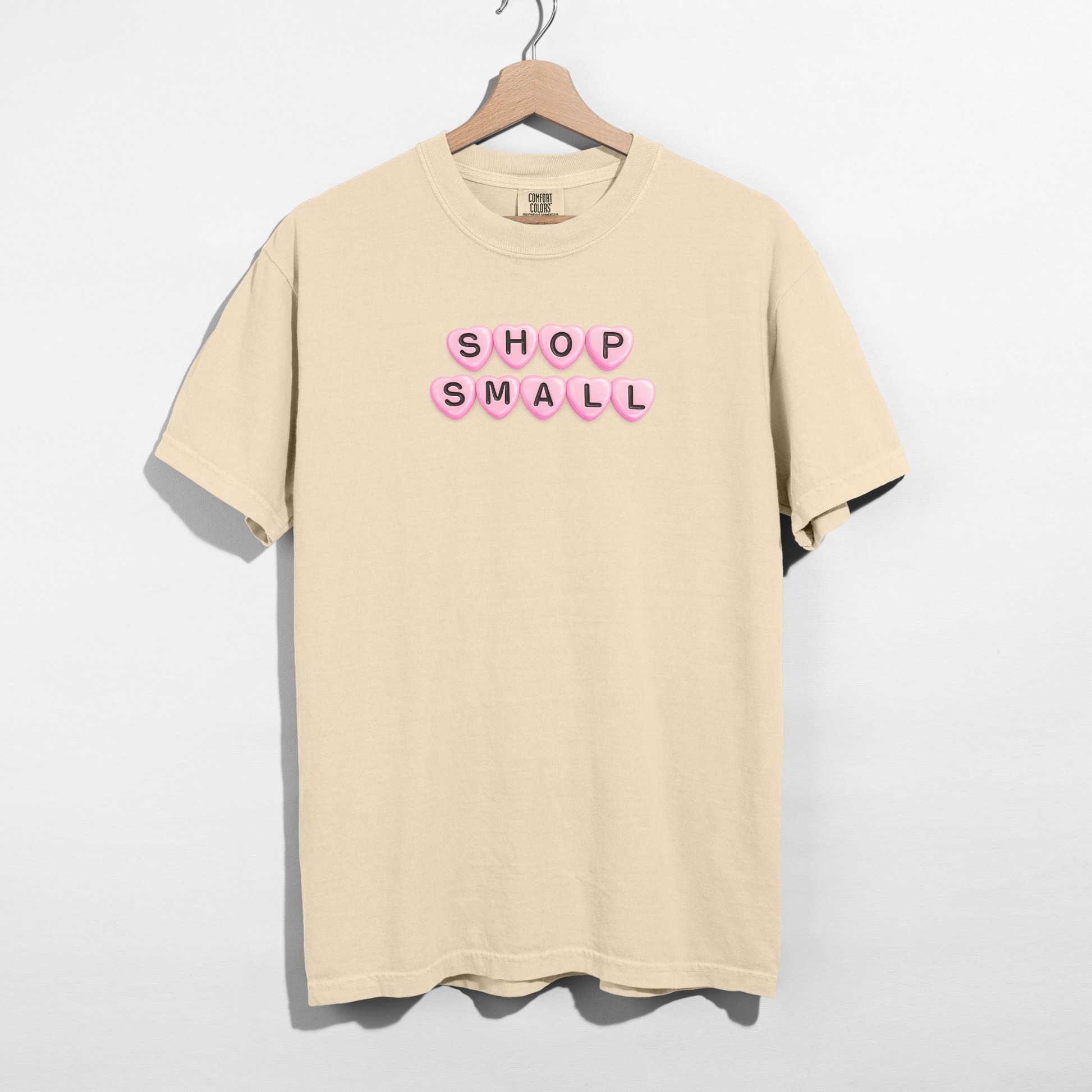 Beige t-shirt with 'SHOP SMALL' text on a hanger against a white background