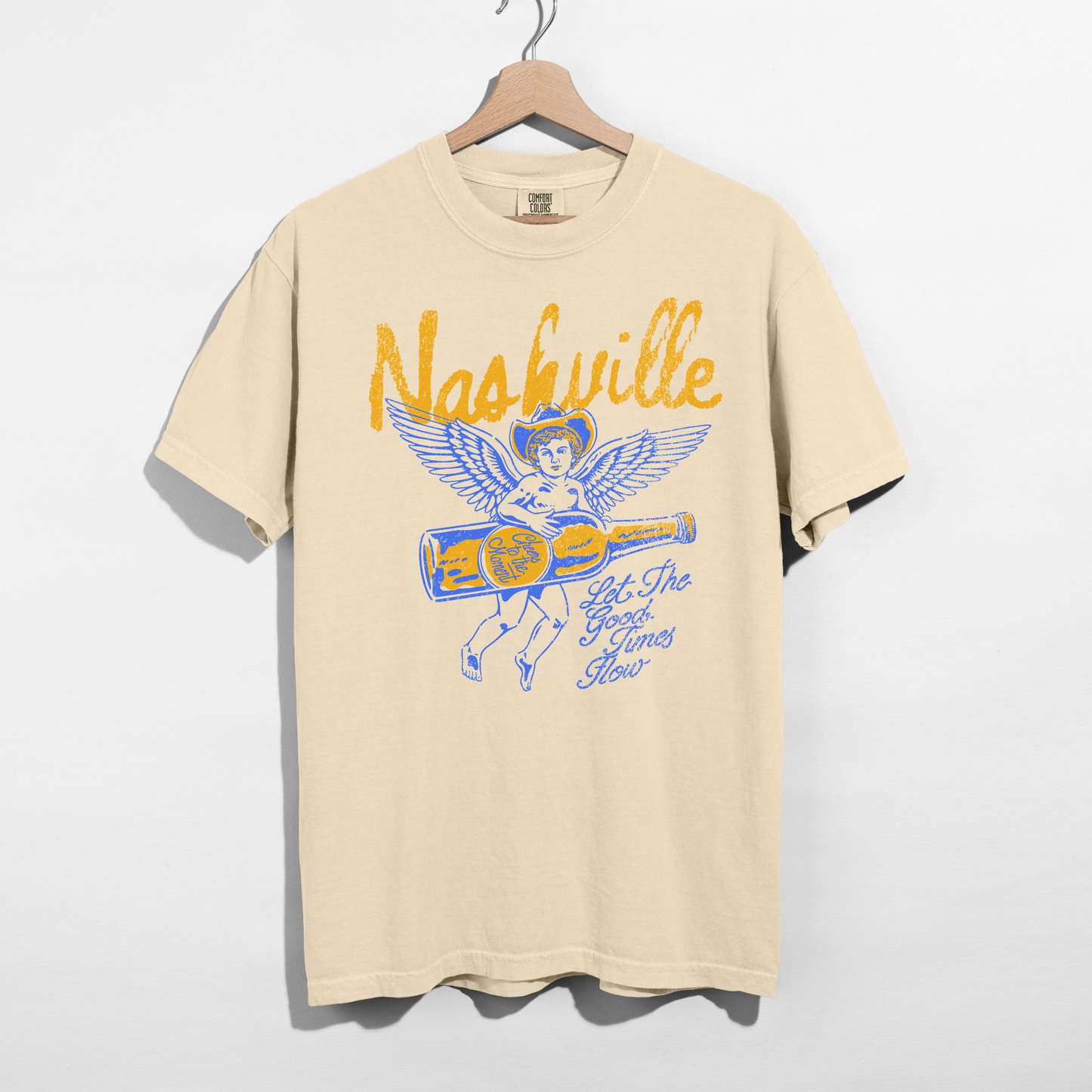 Beige Nashville graphic t-shirt with vintage angel and whiskey bottle design hanging on hanger, western aesthetic shirt