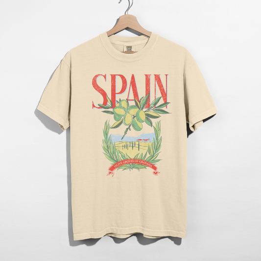 Ivory Comfort Colors Spain graphic tee with olive branches and countryside illustration on hanger