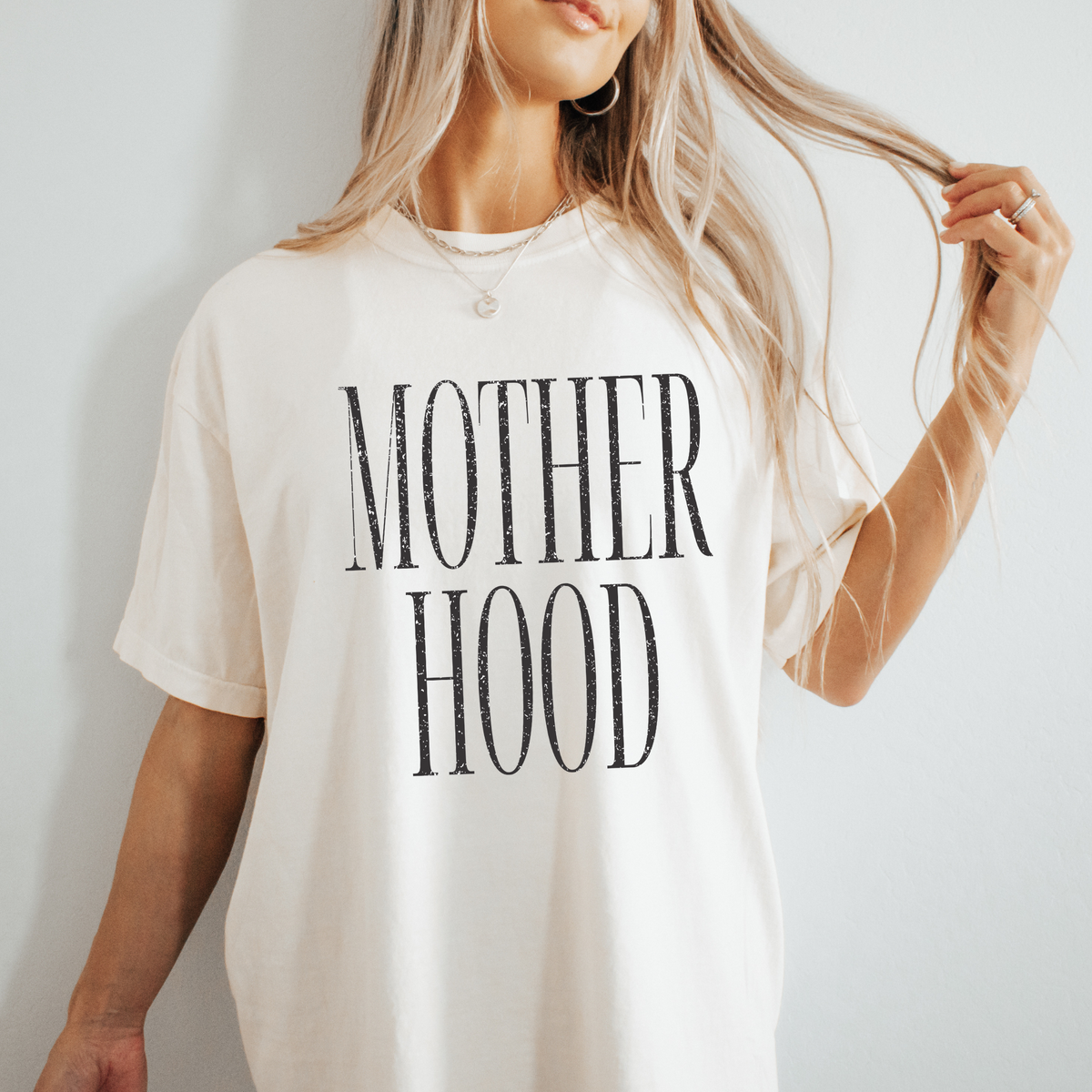 A person wearing a beige t-shirt with the text 'MOTHER HOOD' printed on it.