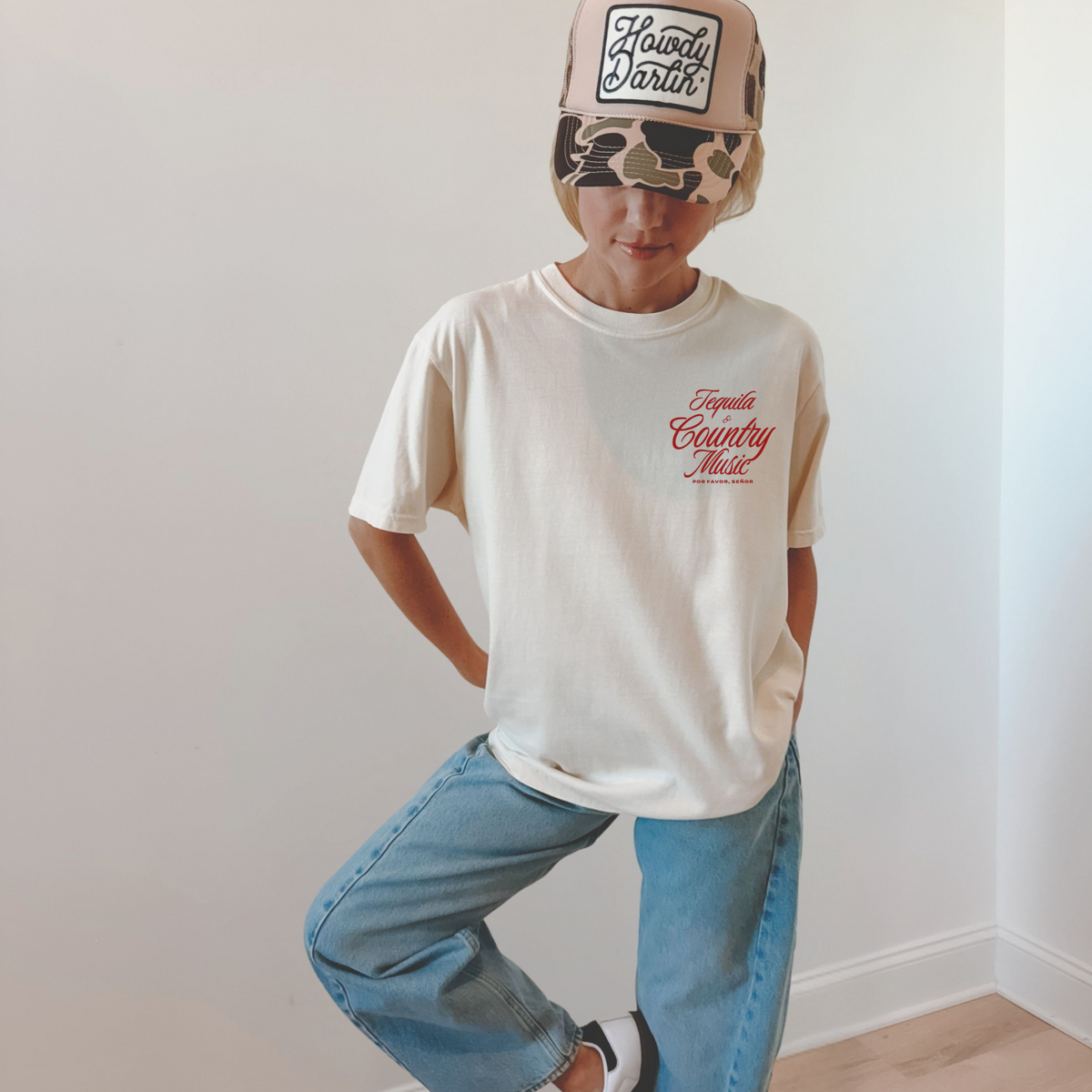 Person wearing a white t-shirt with text and blue jeans against a plain background