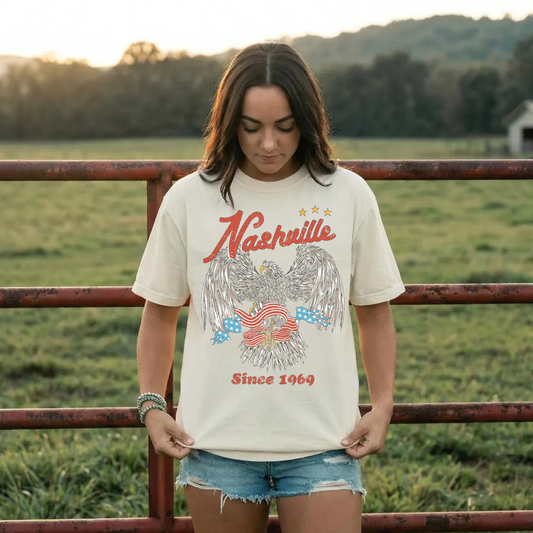 Woman wearing ivory Nashville graphic t-shirt with eagle design and denim shorts western country outfit