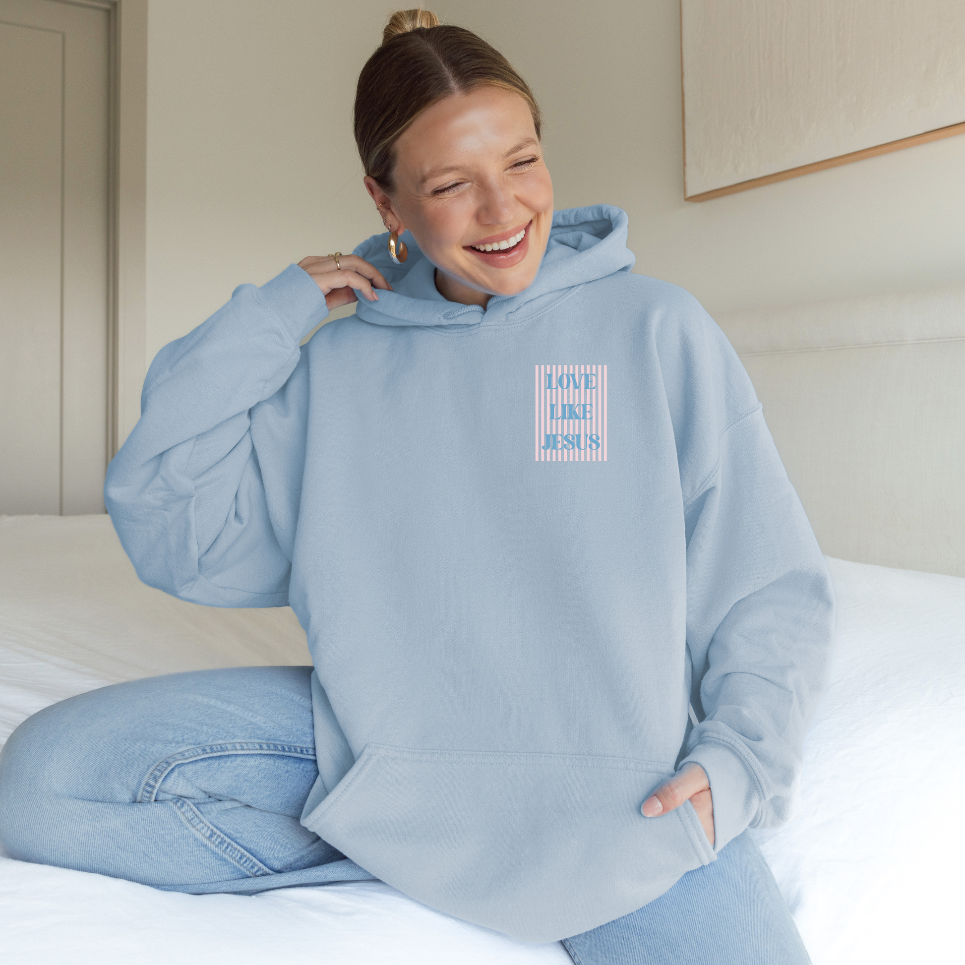 Woman smiling in light blue hoodie with striped front “Love Like Jesus” design.