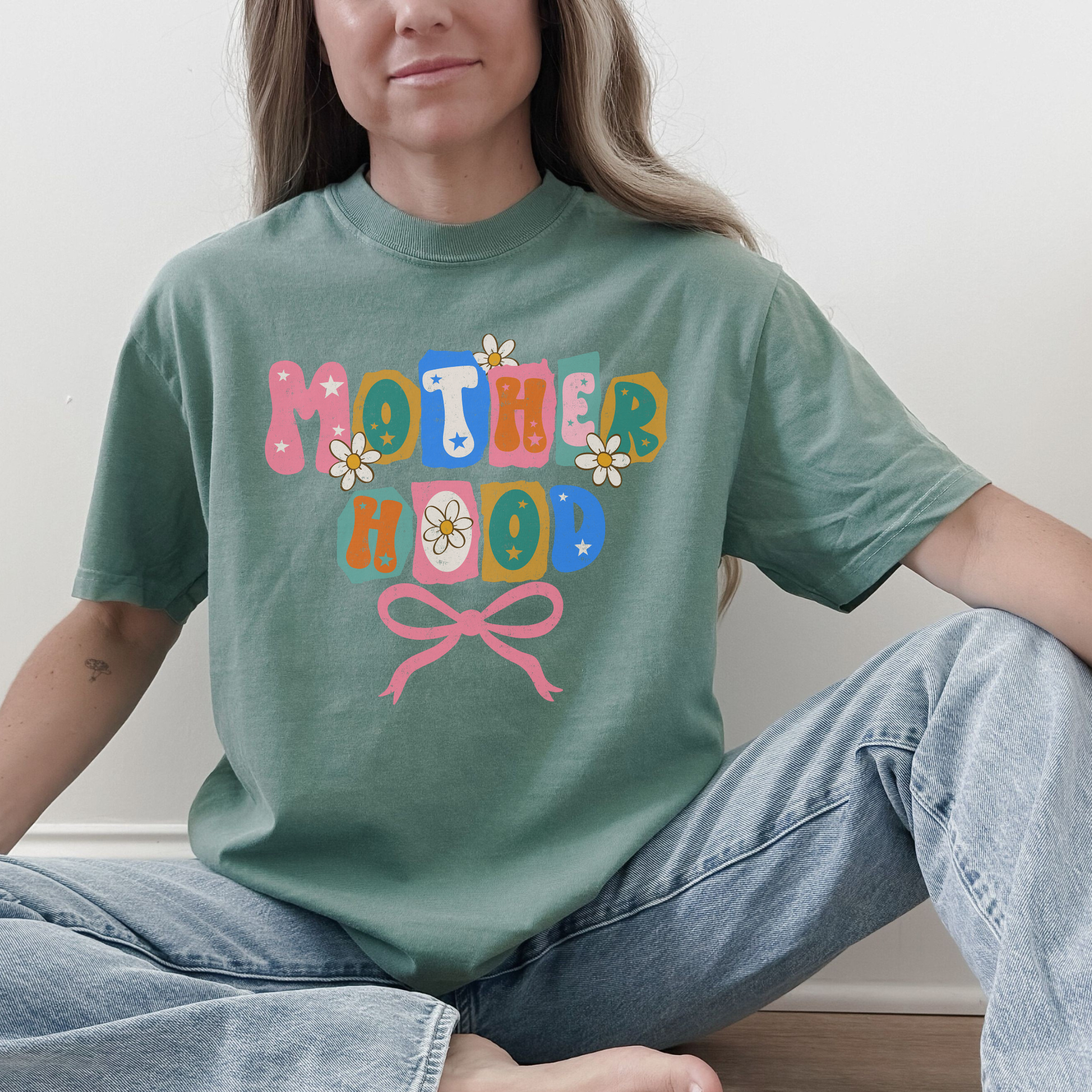 “Woman wearing light green Motherhood retro floral bow graphic tee.”