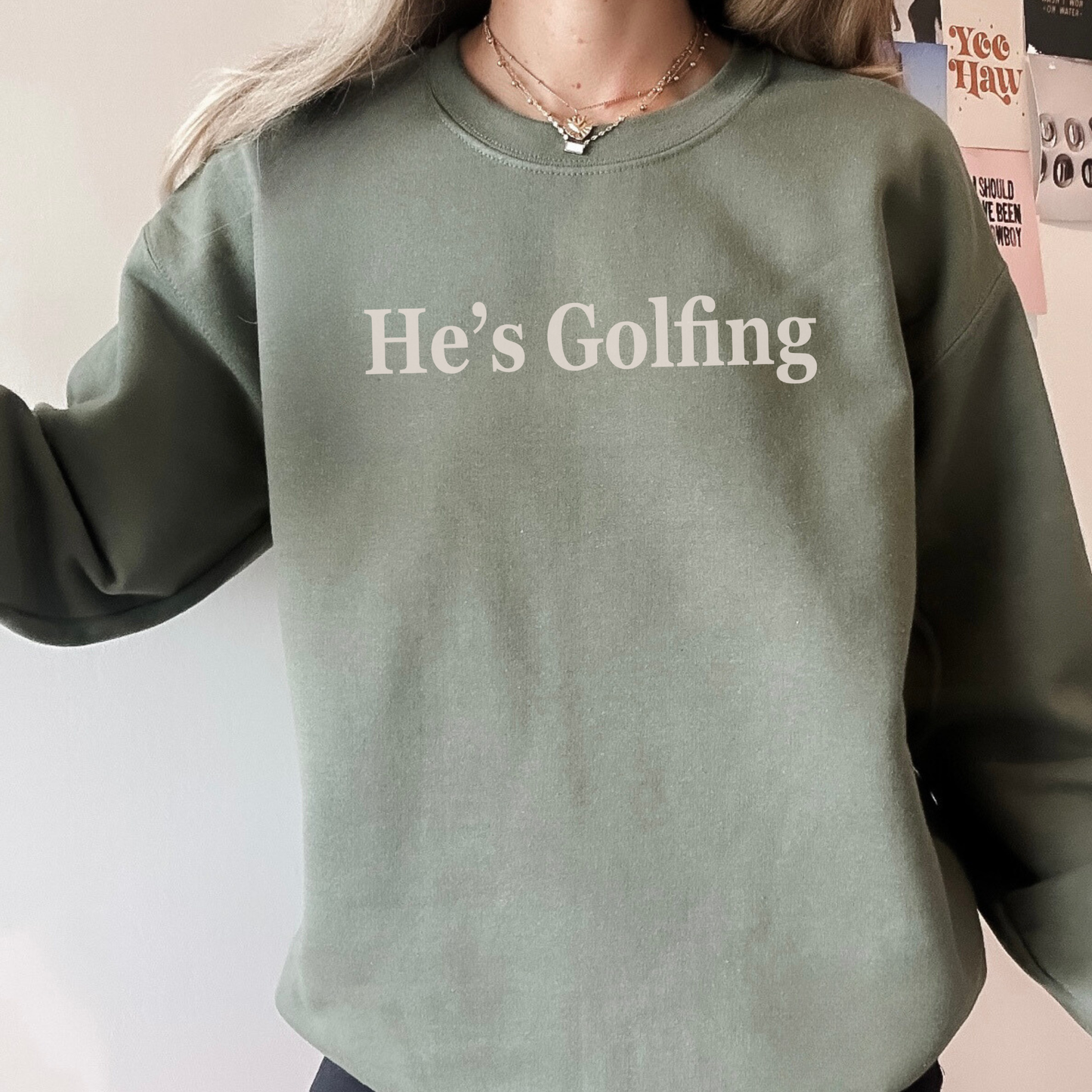 Green sweatshirt with 'He's Golfing' text worn by a person
