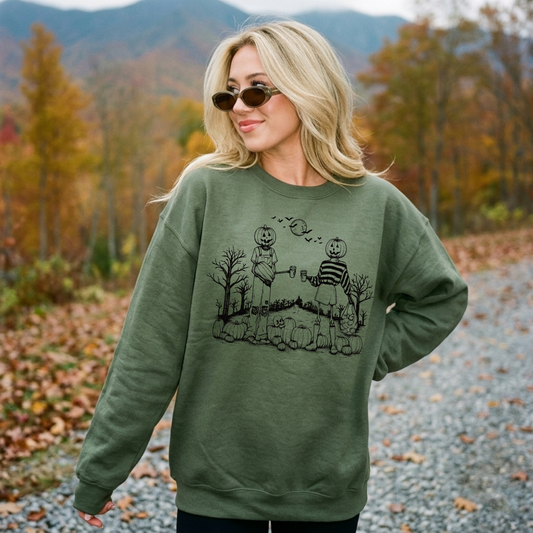 Pumpkin Besties Halloween graphic sweatshirt in military green featuring two pumpkin-headed friends enjoying coffee in a vintage fall scene with pumpkins, bats, and spooky trees.