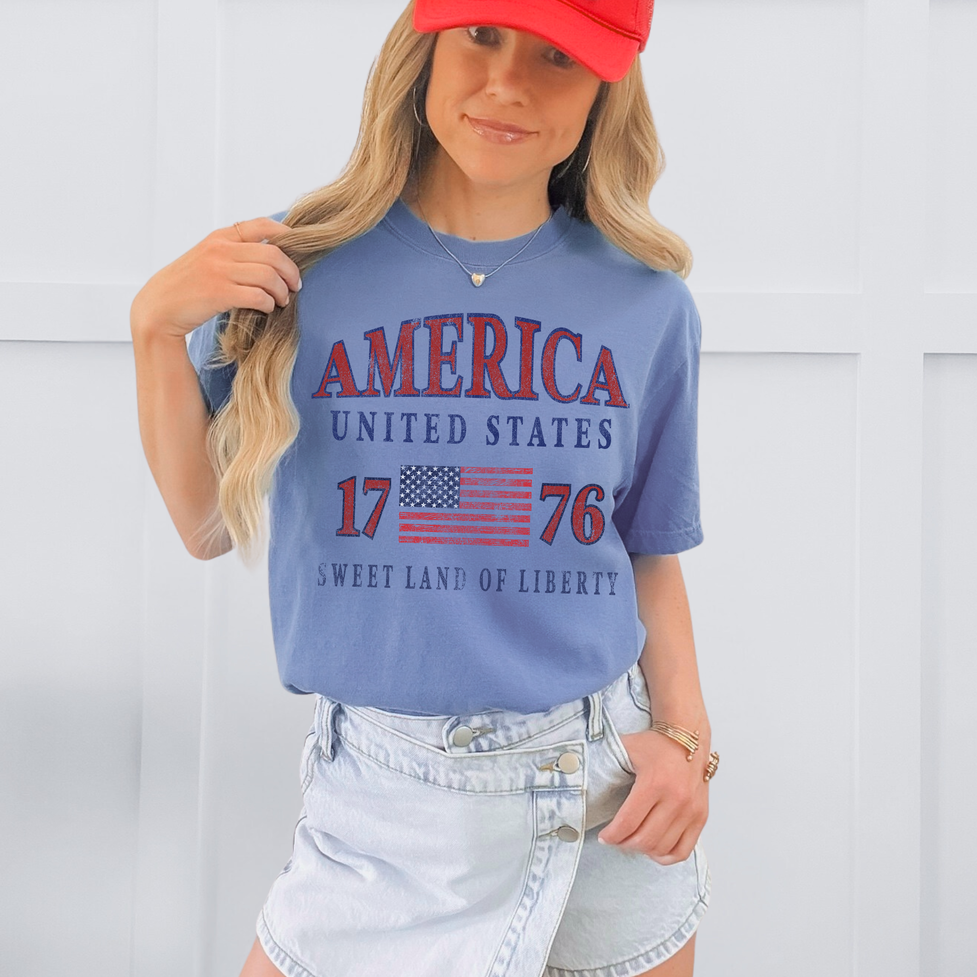 Person wearing a blue t-shirt with 'America United States 1776 Sweet Land of Liberty' text and a red cap.