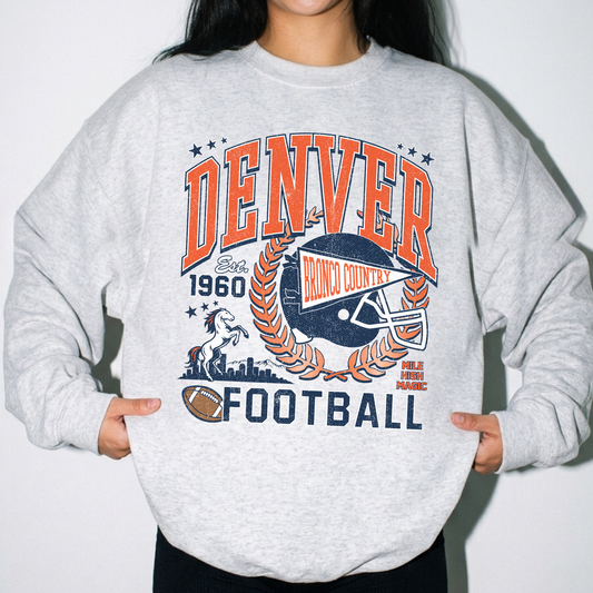 Woman wearing oatmeal heather Denver football sweatshirt with retro orange and navy game day graphic