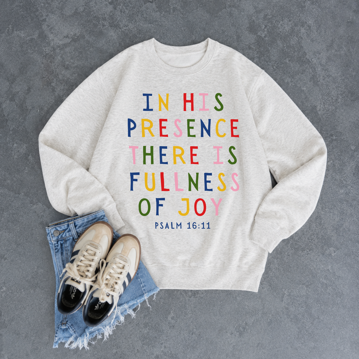 Oatmeal heather Christian crewneck sweatshirt featuring the colorful Bible verse "In His Presence There Is Fullness of Joy" from Psalm 16:11 styled with denim shorts and sneakers.