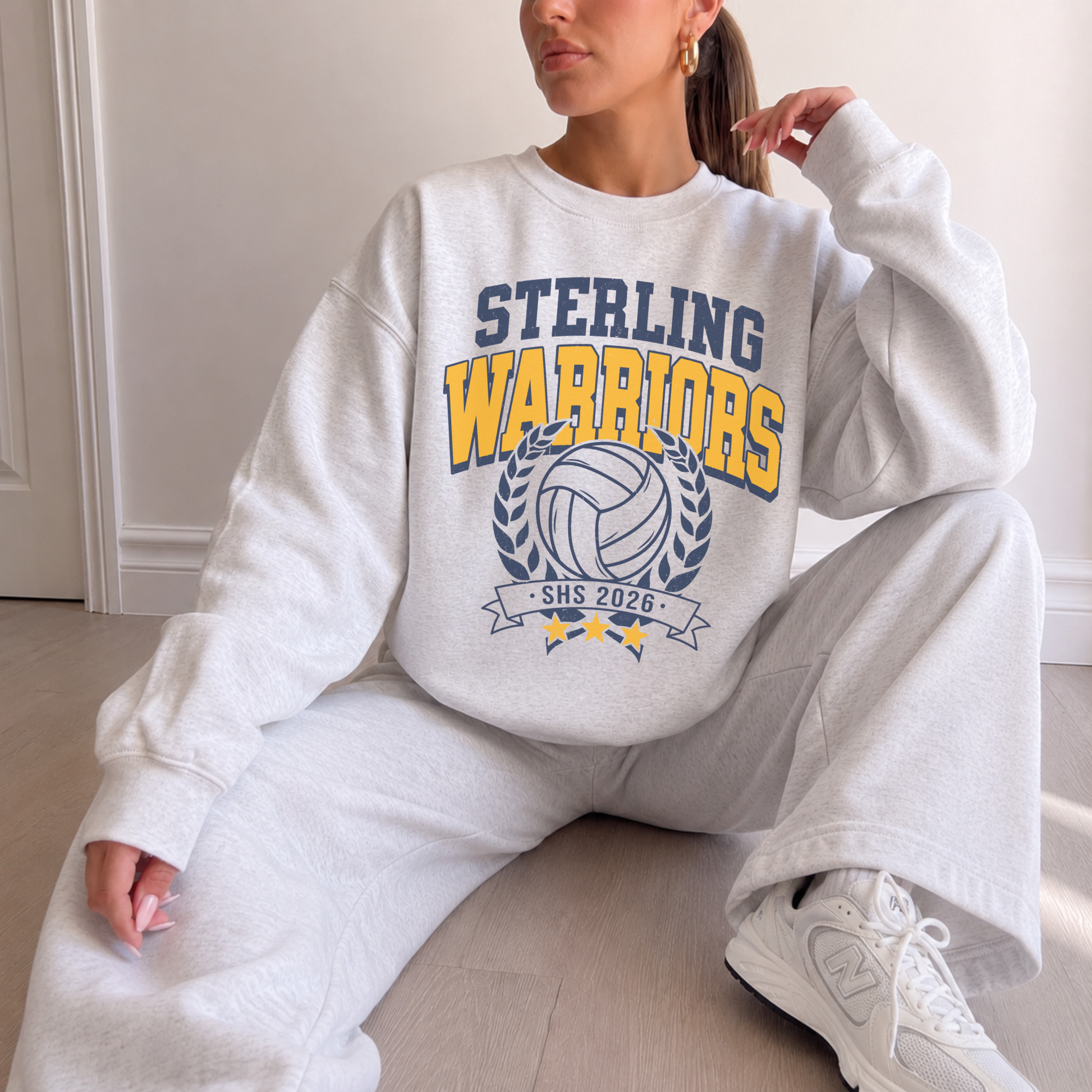 Model wearing an oatmeal heather Sterling Warriors Volleyball 2026 graphic crewneck sweatshirt with matching sweatpants.