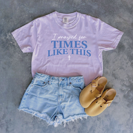 lavender t-shirt with 'I prayed for times like this' text, denim shorts, and tan sandals on a gray surface