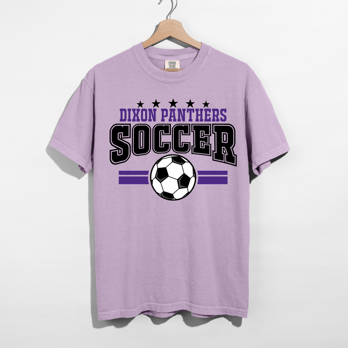 A light purple short-sleeve t-shirt hanging on a wooden hanger against a white wall. The shirt features a graphic print with the text 'DIXON PANTHERS SOCCER' in black and purple, five stars, a soccer ball, and two horizontal purple stripes.